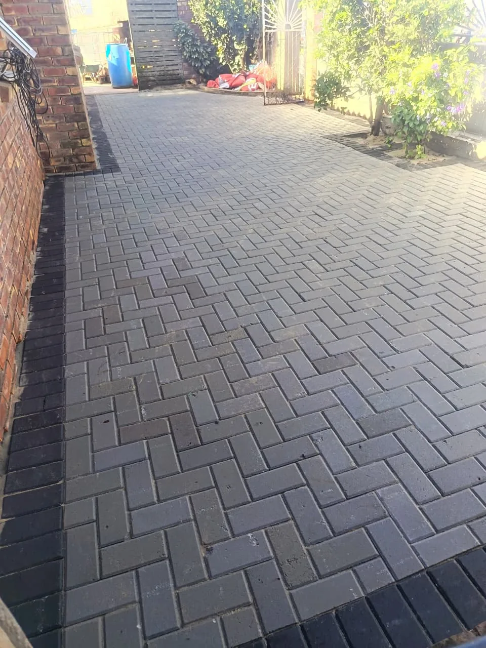 After: the same yard paved as a full-width charcoal herringbone driveway