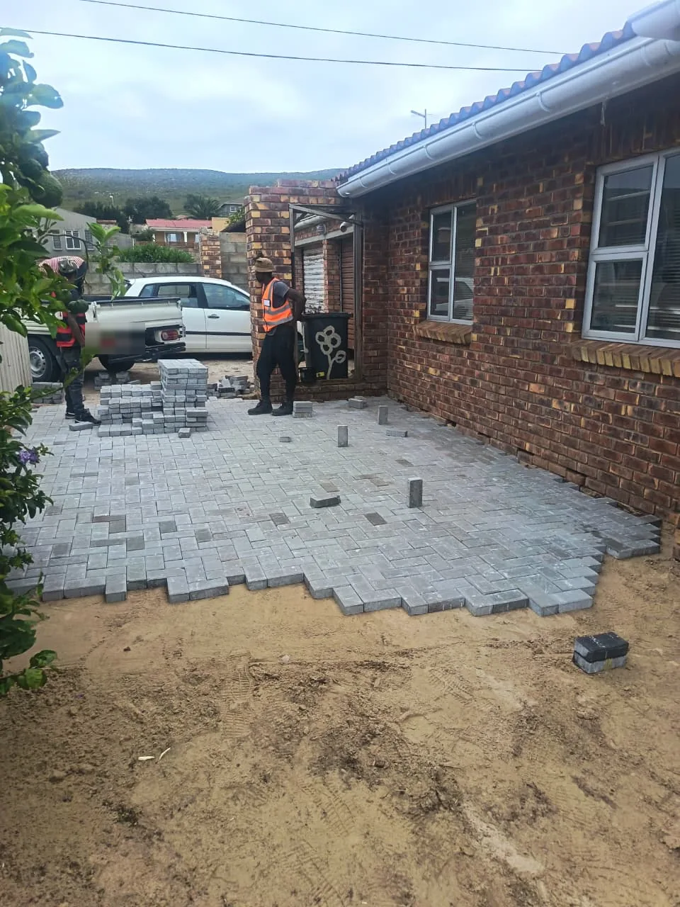Team laying grey pavers in a herringbone pattern, roughly 60 percent complete